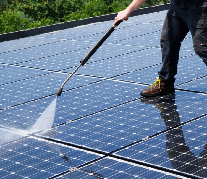 Worker pressure washing rooftop for effective solar panel cleaning