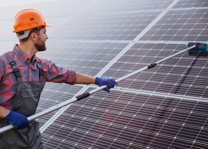 Technician using brush for solar panel cleaning on rooftop installation